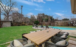 A backyard with a wooden table, outdoor chairs, a swimming pool, and a wooden fence. - Rustic Modern Escape 4-bd/2-ba With Pool & Patio (Houston)
