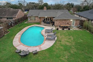 A backyard with a swimming pool, lounge chairs, a barbecue area, and a covered patio. - Rustic Modern Escape 4-bd/2-ba With Pool & Patio (Houston)