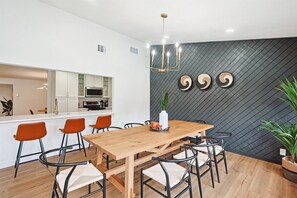Ein moderner Essbereich mit einem Holztisch, orangefarbenen Stühlen und einer Wand mit strukturierter schwarzer Oberfläche.