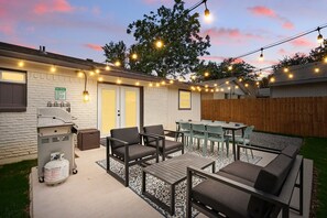 An outdoor patio with a grill, chairs, and tables, surrounded by a wooden fence and a grassy area. - Modern Open-concept 4-bd/3-ba With backyard (Irving)