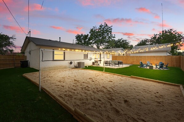 A backyard with a sandpit, a wooden deck, and a house with string lights. - Modern Open-concept 4-bd/3-ba With backyard (Irving)