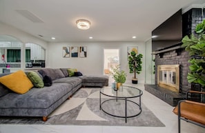 A modern living room with a sectional sofa, a glass coffee table, and a fireplace. - Stunning Modern Dream Home, 5-bd, Sleeps 14 (Houston)
