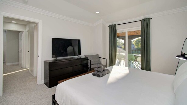 A bedroom with a bed, a TV, a dresser, and a balcony with a view. - Stunning Modern Dream Home, 5-bd, Sleeps 14 (Houston)