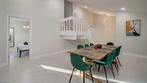 A dining area with a wooden table, green chairs, a white staircase, and a modern art piece on the wall. - Stunning Modern Dream Home, 5-bd, Sleeps 14 (Houston)