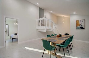 A dining area with a wooden table, green chairs, a white staircase, and a modern art piece on the wall. - Stunning Modern Dream Home, 5-bd, Sleeps 14 (Houston)