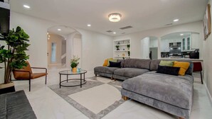 A modern living room with a grey sectional sofa, a round coffee table, and a potted plant. - Stunning Modern Dream Home, 5-bd, Sleeps 14 (Houston)