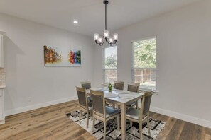 Ein Essbereich mit einem für sechs Personen gedecktem Tisch, einer Chandelierleuchtre und zwei Fenstern mit Jalousien.