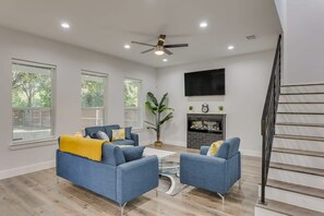 Ein geräumiges Wohnzimmer mit Kamin, zwei blauen Sofas, einem Couchtisch und einem Deckenventilator.