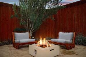 A fire pit with two chairs, a wooden fence, and a tree in a backyard. - Best of Allen at Fountain Park 5-bd/2-ba w/ Pool (Allen)