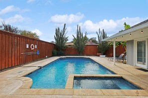A rectangular swimming pool with a wooden deck surrounding it, a covered patio area with chairs, and a fenced backyard. - Best of Allen at Fountain Park 5-bd/2-ba w/ Pool (Allen)