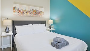 A hotel room with a bed, two bedside tables with lamps, a wall painting, and a blue and yellow accent wall. - Best of Allen at Fountain Park 5-bd/2-ba w/ Pool (Allen)
