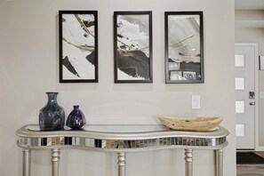 A hallway with three framed abstract paintings, a console table with two vases, and a wooden bowl. - Best of Allen at Fountain Park 5-bd/2-ba w/ Pool (Allen)