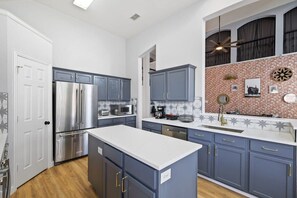A modern kitchen with stainless steel appliances, blue cabinets, and a brick accent wall. - Stylish, Spacious, Convenient - 6-bd/2.5-ba + Pool (Fort Worth)