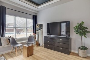 Ein modernes Wohnzimmer mit großem Fernseher, einer Couch, zwei Sesseln, einem Couchtisch aus Holz und einer Topfpflanze.