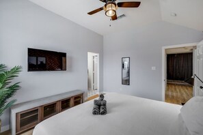 A bedroom with a bed, a ceiling fan, a TV mounted on the wall, and a door leading to another room. - Stylish, Spacious, Convenient - 6-bd/2.5-ba + Pool (Fort Worth)