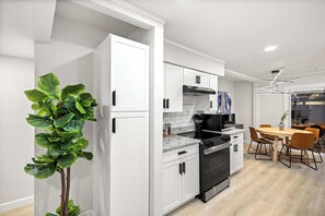 Eine moderne Küche mit weißen Schränken, einem schwarzen Backofen und einem Essbereich mit Holztischen und -stühlen.