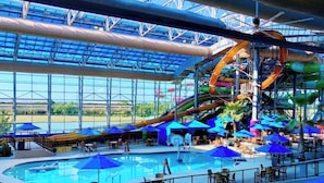 An indoor water park with a large pool, slides, and umbrellas. - 5-bd/2.5-ba Modern Retreat w/ Games (Grand Prairie)