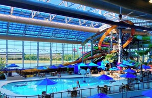 Ein großer Indoor-Wasserpark mit Schwimmbecken, Rutschen und Sonnenschirmen.