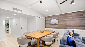 A modern dining area with a wooden table and chairs, a ceiling fan, and a television mounted on the wall. - 5-bd/2.5-ba Modern Retreat w/ Games (Grand Prairie)