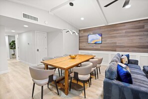 Ein moderner Essbereich mit Holztisch und -stühlen, einem Deckenventilator und einem an der Wand montierten Fernseher.