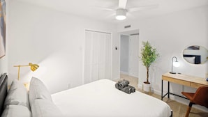 A bedroom with a bed, a desk, a chair, a ceiling fan, a potted plant, and a mirror. - 5-bd/2.5-ba Modern Retreat w/ Games (Grand Prairie)