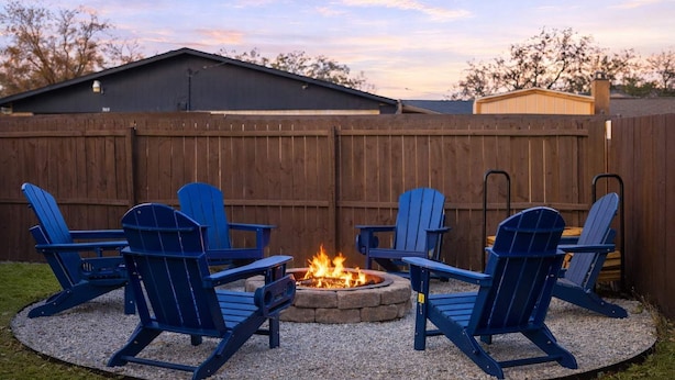 A backyard with four blue Adirondack chairs arranged around a stone fire pit. - 5-bd/2.5-ba Modern Retreat w/ Games (Grand Prairie)
