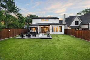 A two-story house with a backyard patio, a covered outdoor seating area, and a visible chimney. - 6bd/5ba of Modern Elegance Cinema, Games, Hottub (Dallas)