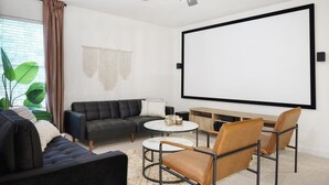 A modern living room with a large flat-screen TV, a ceiling fan, a sofa, a coffee table, and a chair. - Live Like Royalty - Highland Village 6BR Mansion (Lewisville)