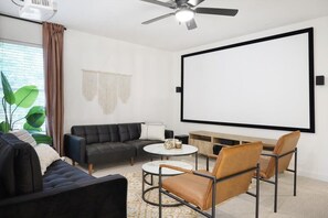 A living room with a sofa, armchair, coffee table, and a projector screen. - Live Like Royalty - Highland Village 6BR Mansion (Lewisville)