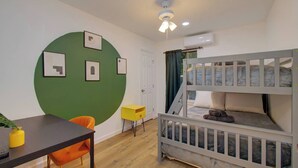 Ein Zimmer mit Etagenbetten, einem Schreibtisch, Stühlen, einer grünen Wand mit Bildern und einem Deckenventilator.