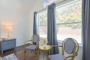 A room with two chairs, a small round table with a vase, a lamp, and a window with curtains. - The Blue Holly - Bright & Spacious With a Pool (Denton)