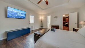 Ein Schlafzimmer mit einem großen Bett, einem Deckenventilator, einem an der Wand montierten Fernseher, einer Bank und einem begehbaren Kleiderschrank.