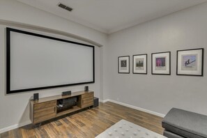 A modern living room with a large flat-screen TV, a wooden entertainment unit, a grey sofa, and framed pictures on the wall. - Spacious and Luxury Home w/ Cinema Room and Pool (Grand Prairie)