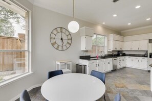 A modern kitchen with white cabinets, a round table, and a large wall clock. - Spacious and Luxury Home w/ Cinema Room and Pool (Grand Prairie)