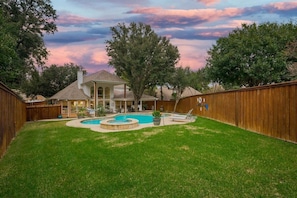 A backyard with a swimming pool, a covered patio, and a wooden fence. - Spacious and Luxury Home w/ Cinema Room and Pool (Grand Prairie)
