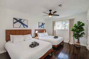 A hotel room with two beds, a ceiling fan, artwork on the walls, a window with curtains, and a potted plant. - 4-bd Mid-modern Century With Firepit & Playground (Houston)