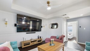 Uma sala de estar moderna com uma grande televisão de tela plana, uma mesa de centro de madeira, um sofá verde-água e uma poltrona rosa.