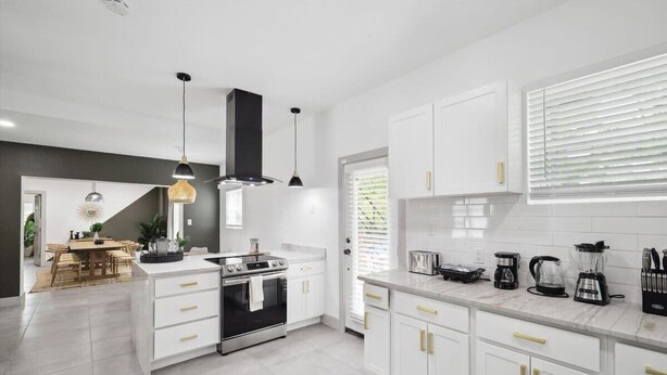 A modern kitchen with white cabinets, a stove, and a dining area with a table and chairs. - Tropical Oasis - Pool + Beach Volleyball + Firepit (Lancaster)