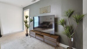 A living room with a flat-screen TV, a wooden entertainment unit, and two potted plants. - Tropical Oasis - Pool + Beach Volleyball + Firepit (Lancaster)