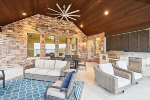 A covered patio with wicker furniture, a brick wall, and a kitchen area. - Lakefront Mansion With Pool and Cinema (Wylie)