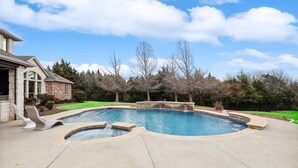 A backyard with a swimming pool, a stone waterfall feature, and a house with a stone facade. - Lakefront Mansion With Pool and Cinema (Wylie)
