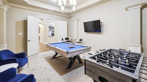 A room with a pool table, blue chairs, a foosball table, a TV, and a door leading to another room. - Lakefront Mansion With Pool and Cinema (Wylie)