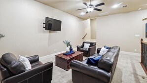 A living room with a flat-screen TV, a ceiling fan, and a brown coffee table. - Lakefront Mansion With Pool and Cinema (Wylie)