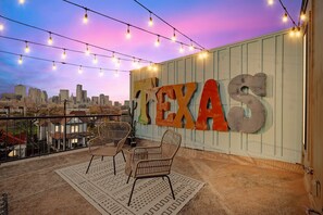 A balcony with string lights, a large 'TEXAS' sign, wicker chairs, and a city skyline view. - Best of The Cedars - Dallas Views, Rooftop Luxury (Dallas)