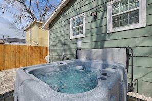 Ein Whirlpool vor einem Haus mit Holzzaun und blauem Himmel.