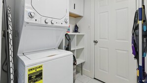 Un área de lavandería con lavadora y secadora, un estante con productos de limpieza y una puerta.