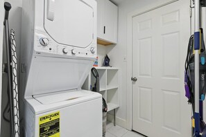 A laundry area with a washer and dryer, a shelf with cleaning supplies, and a door. - Charming Historic 3B Heart of Dallas - Sleeps 12 (Dallas)