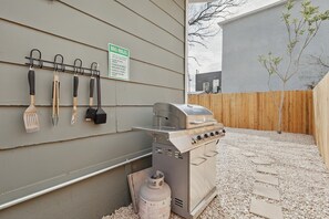 A barbecue grill with a gas tank, a set of utensils hanging on a wall, and a sign with BBQ rules. - Charming Historic 3B Heart of Dallas - Sleeps 12 (Dallas)