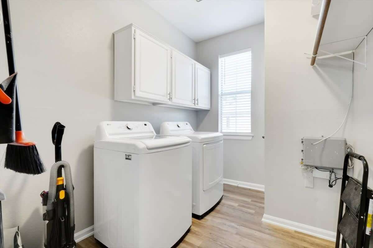 A laundry room with two white front-loading washers and dryers, a broom, and a vacuum cleaner.