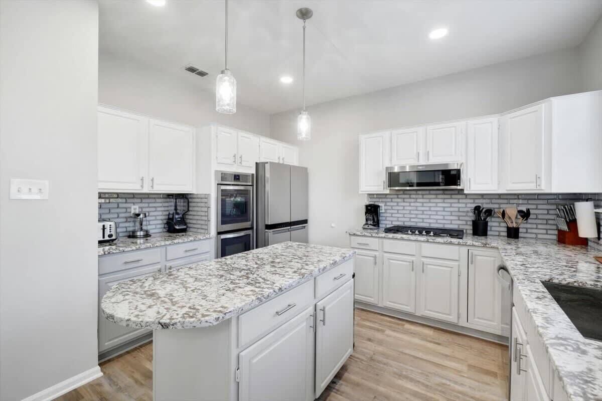 A modern kitchen with white cabinets, granite countertops, stainless steel appliances, and pendant lighting.